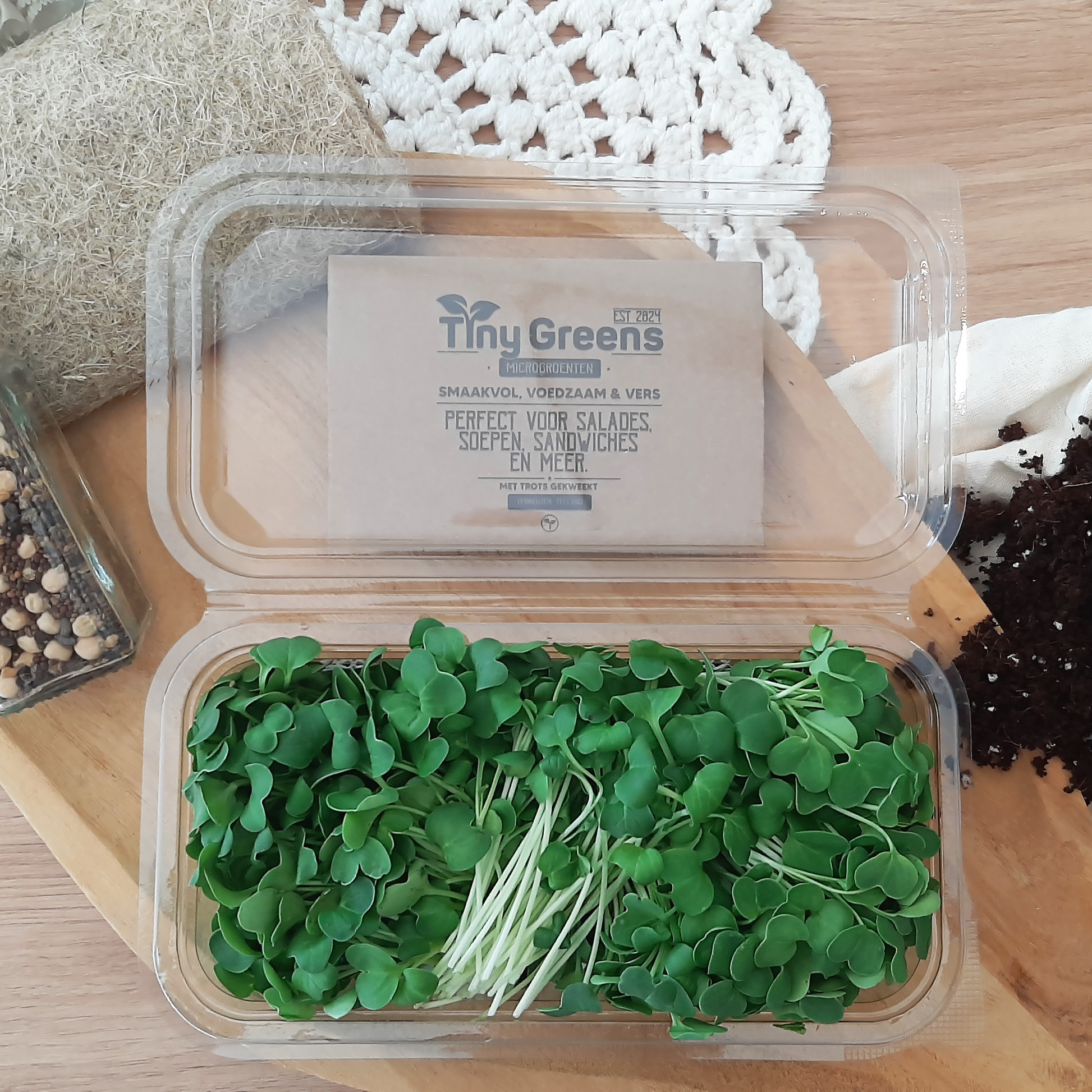 Natuurlijke daikon radijs cress van TinyGreens, biologisch verantwoord geteeld en rijk aan voedingsstoffen, perfect voor salades en als garnering. Gepresenteerd als bovenaanzicht in doorzichtig plastic schaal, met het label van TinyGreens er zichtbaar achter.