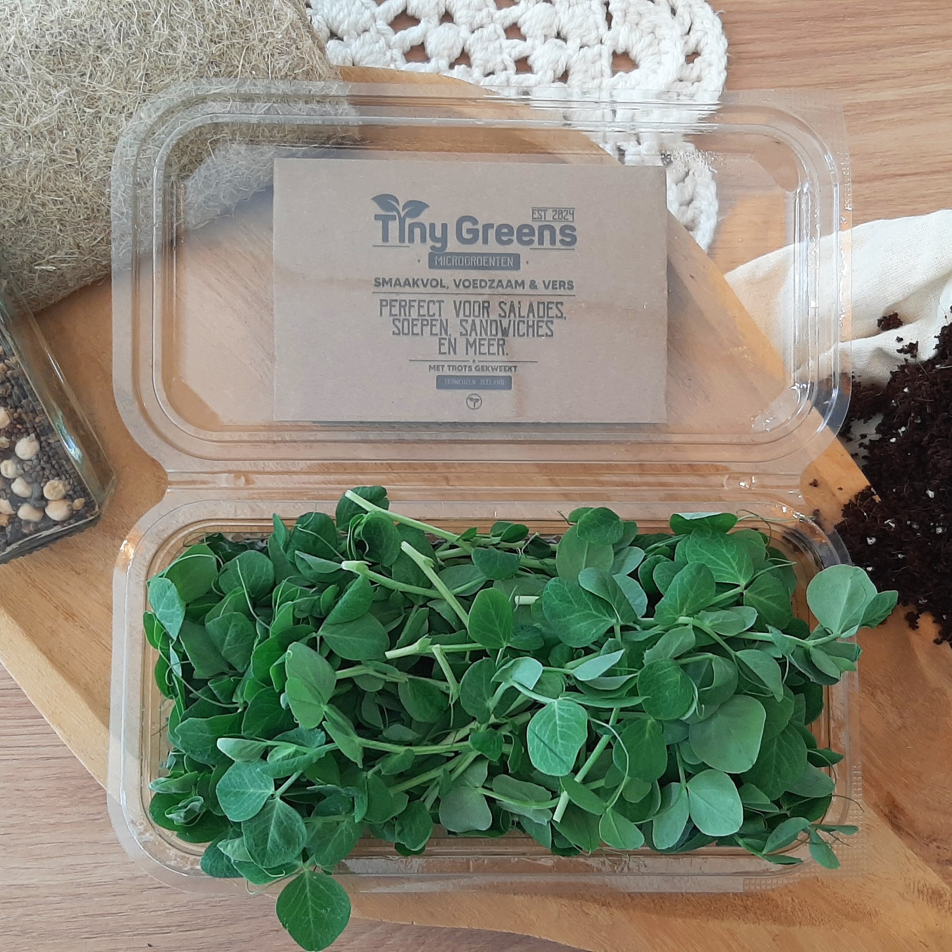 Natuurlijke doperwt cress van TinyGreens, biologisch verantwoord geteeld en rijk aan voedingsstoffen, perfect voor salades en als garnering. Gepresenteerd als bovenaanzicht in doorzichtig plastic schaal, met het label van TinyGreens er zichtbaar achter.