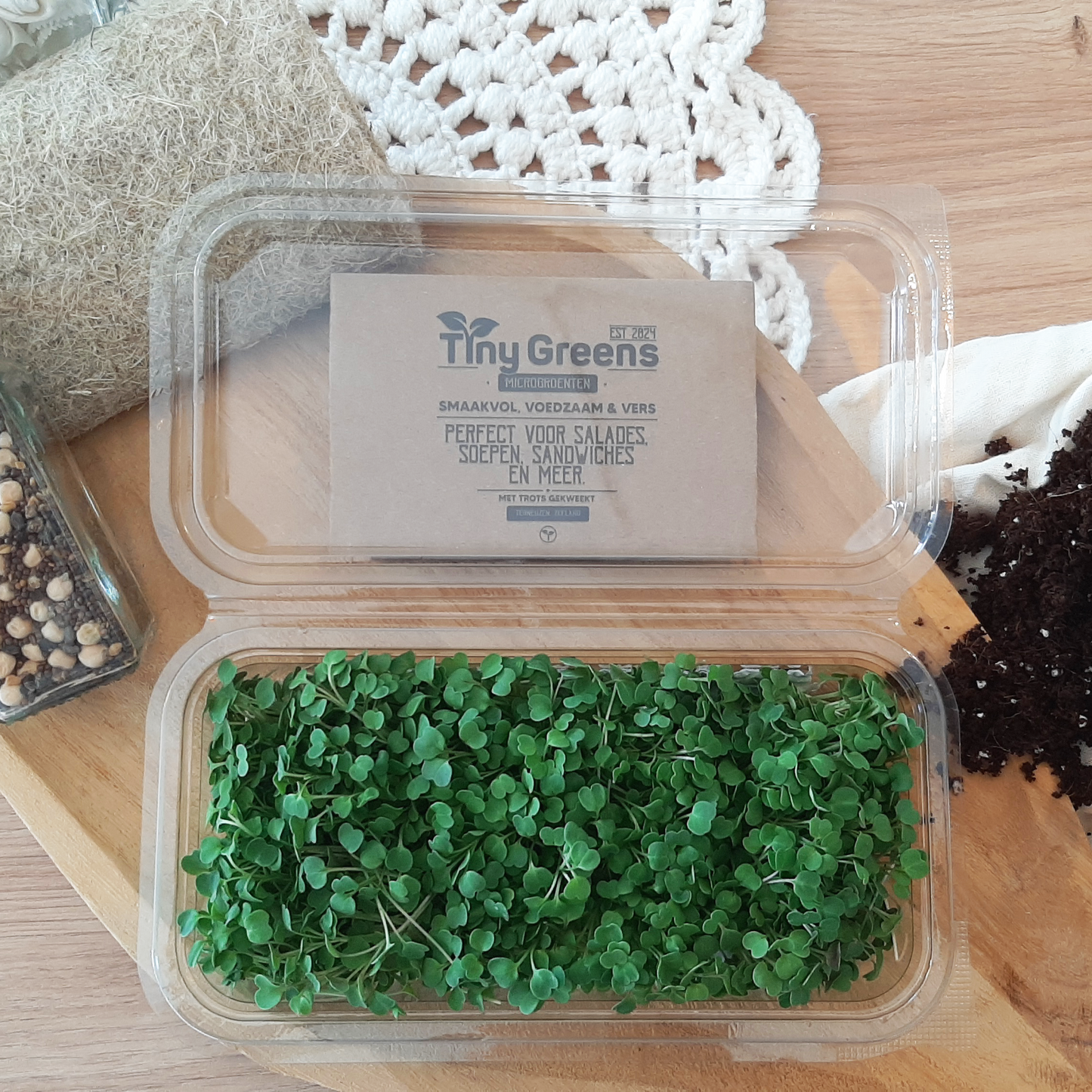 Natuurlijke rucola cress van TinyGreens, biologisch verantwoord geteeld en rijk aan voedingsstoffen, perfect voor salades en als garnering. Gepresenteerd als bovenaanzicht in doorzichtig plastic schaal, met het label van TinyGreens er zichtbaar achter.